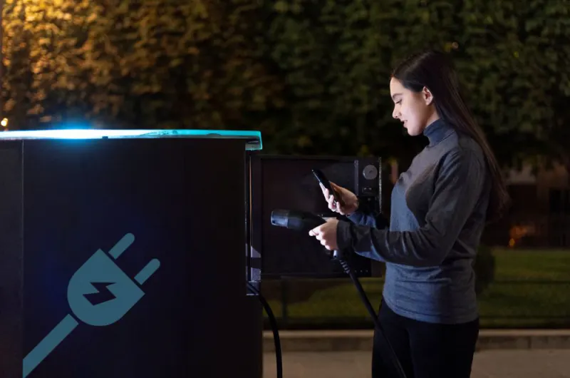Mulher a carregar um veículo elétrico com energia renovável